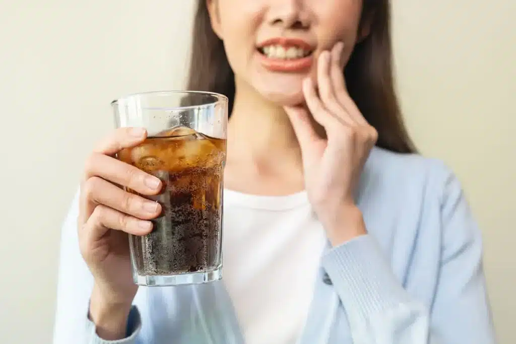 Woman holding a glass and showing her teeth in pain due to tooth sensitivity in cold weather